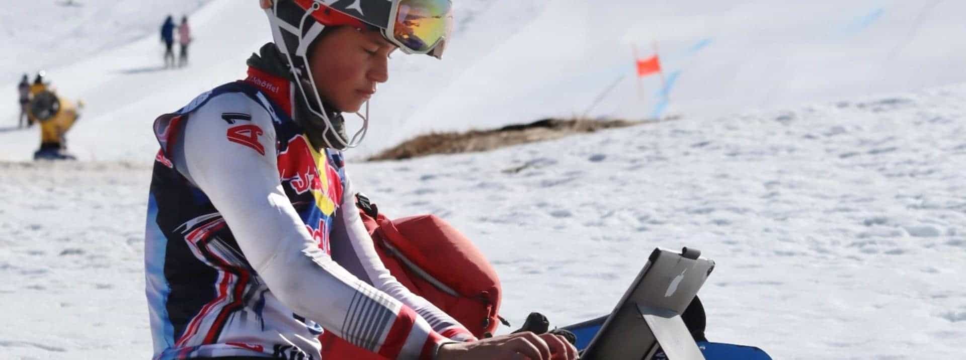 Young skier using a laptop outdoors on snowy mountain, preparing for winter sports at World Schools.