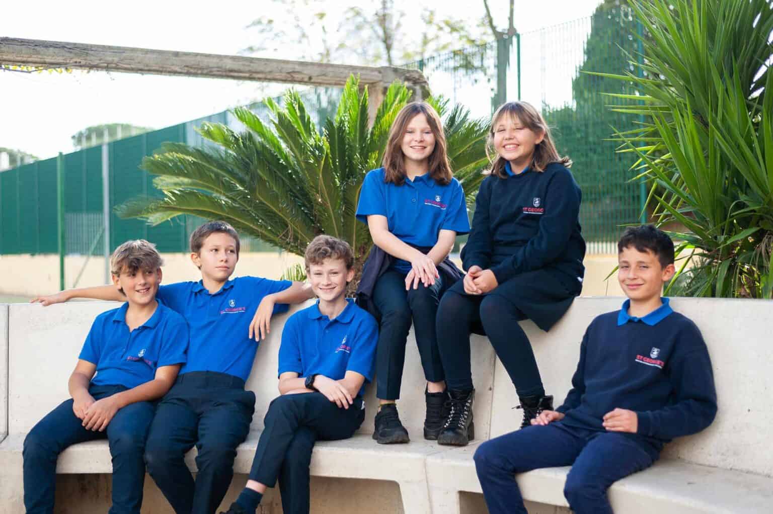 Studenti in uniforme scolastica seduti all'aperto su una panchina in un giardino rigoglioso di una scuola mondiale.