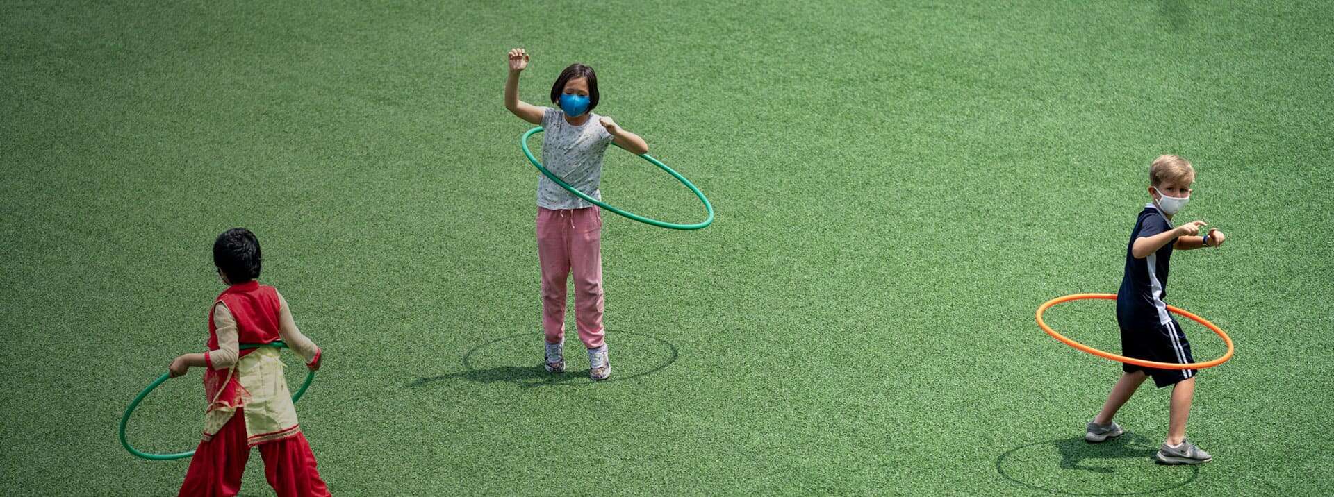 Bright children playing with hula hoops on green school playground, fostering physical activity and social skills.