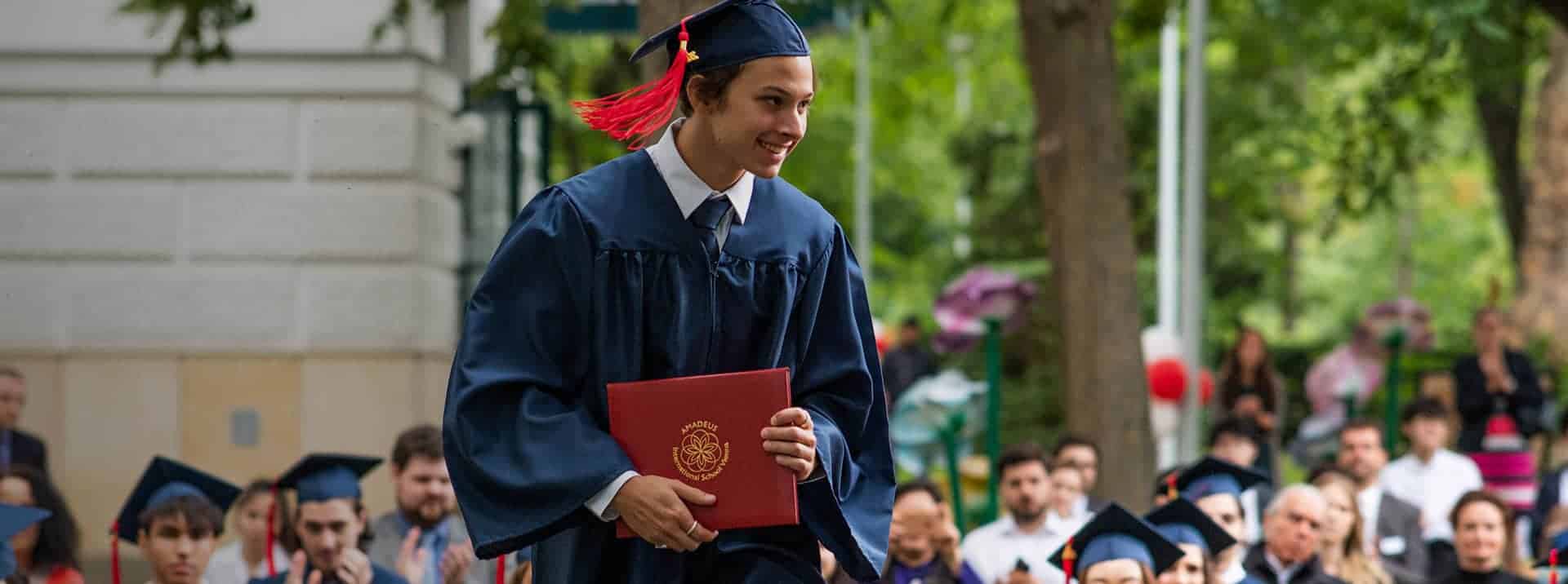Graduate student in cap and gown receives diploma at outdoor graduation ceremony.