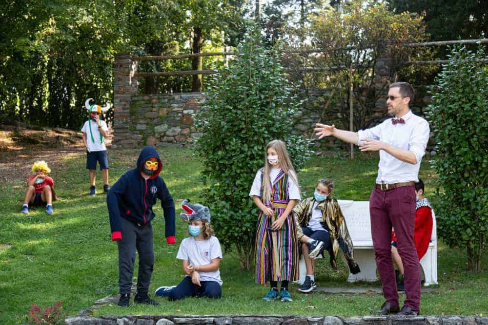 Vibrant outdoor school play with children in costumes and teacher conducting activity at World Schools Open Air Classroom.
