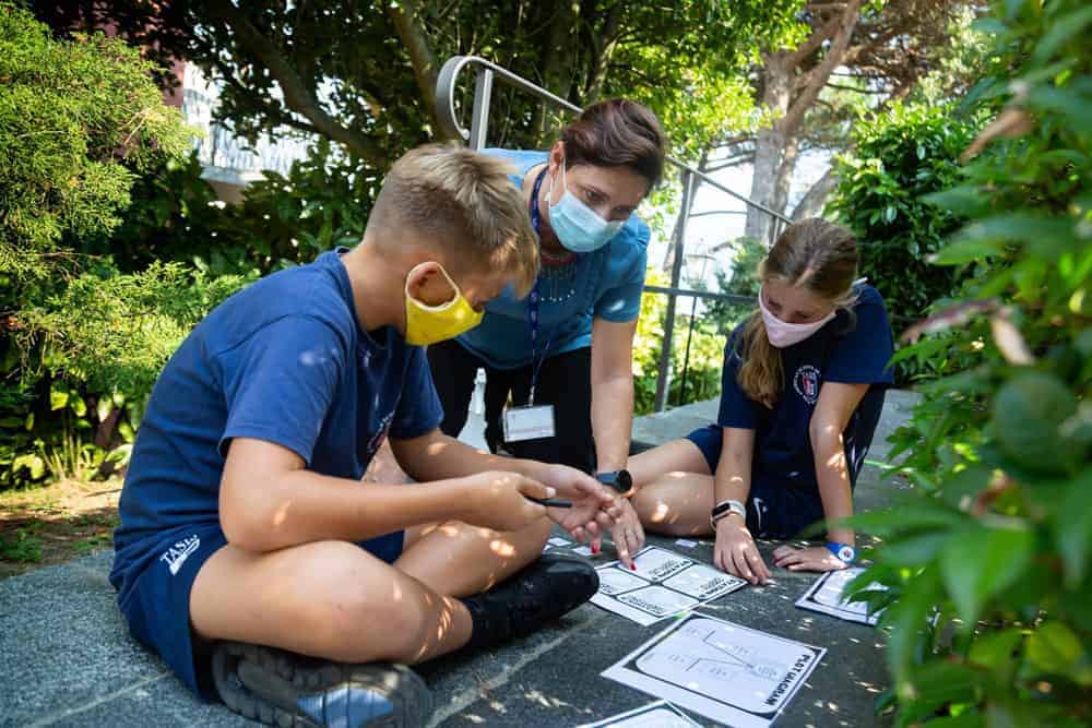 Students with teacher discussing educational worksheets outdoors, promoting innovative learning at World Schools.