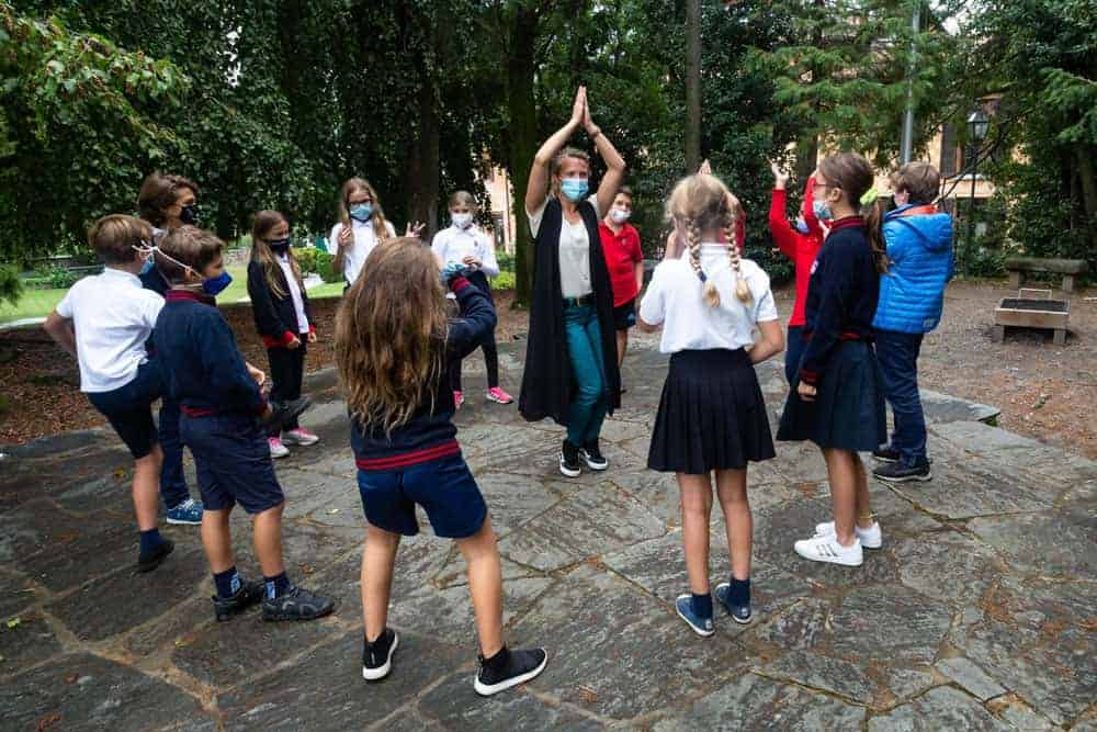 Children practicing outdoor yoga in schoolyard with teacher, kids wearing masks, healthy activity at World Schools event on safety and wellness.