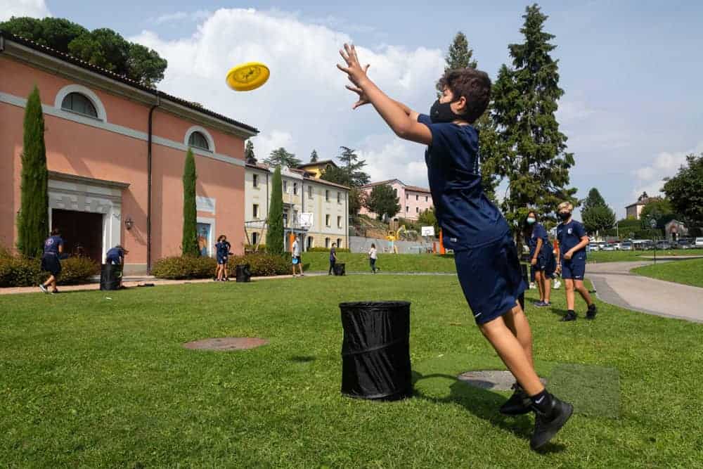 Kids playing outdoor games at World Schools. Child throwing a frisbee in a sunny schoolyard. Engaging activities for students' development and fun.
