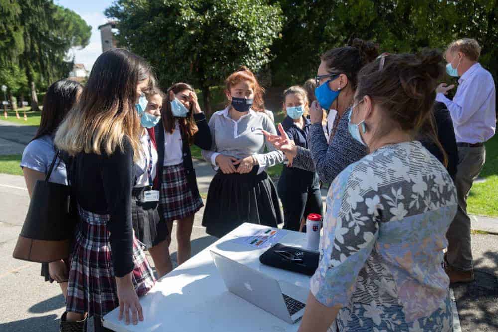 Students and teachers discussing outdoors at World Schools event, wearing masks, promoting global education.