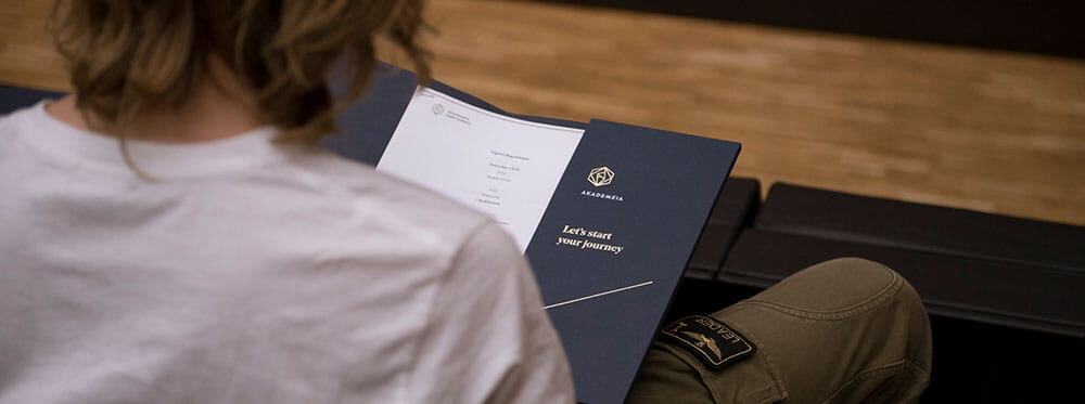 Highly detailed student reading academic booklet at World Schools music room with a backpack nearby.