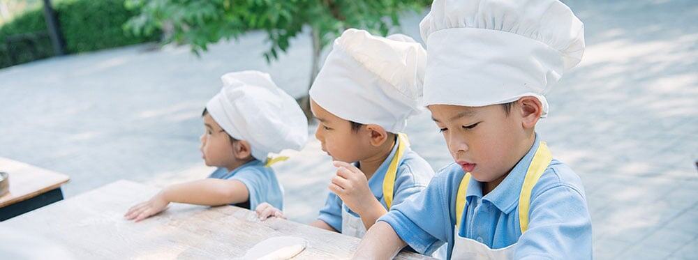 Children in chef hats participating in outdoor cooking activity at a school event.
