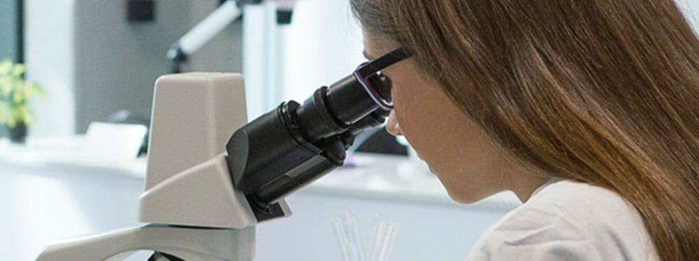 High school student using a microscope for science class in a modern laboratory setting.