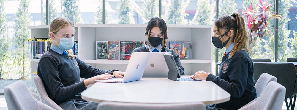 Bright students studying collaboratively at a world school library with laptops and books, fostering global education excellence.