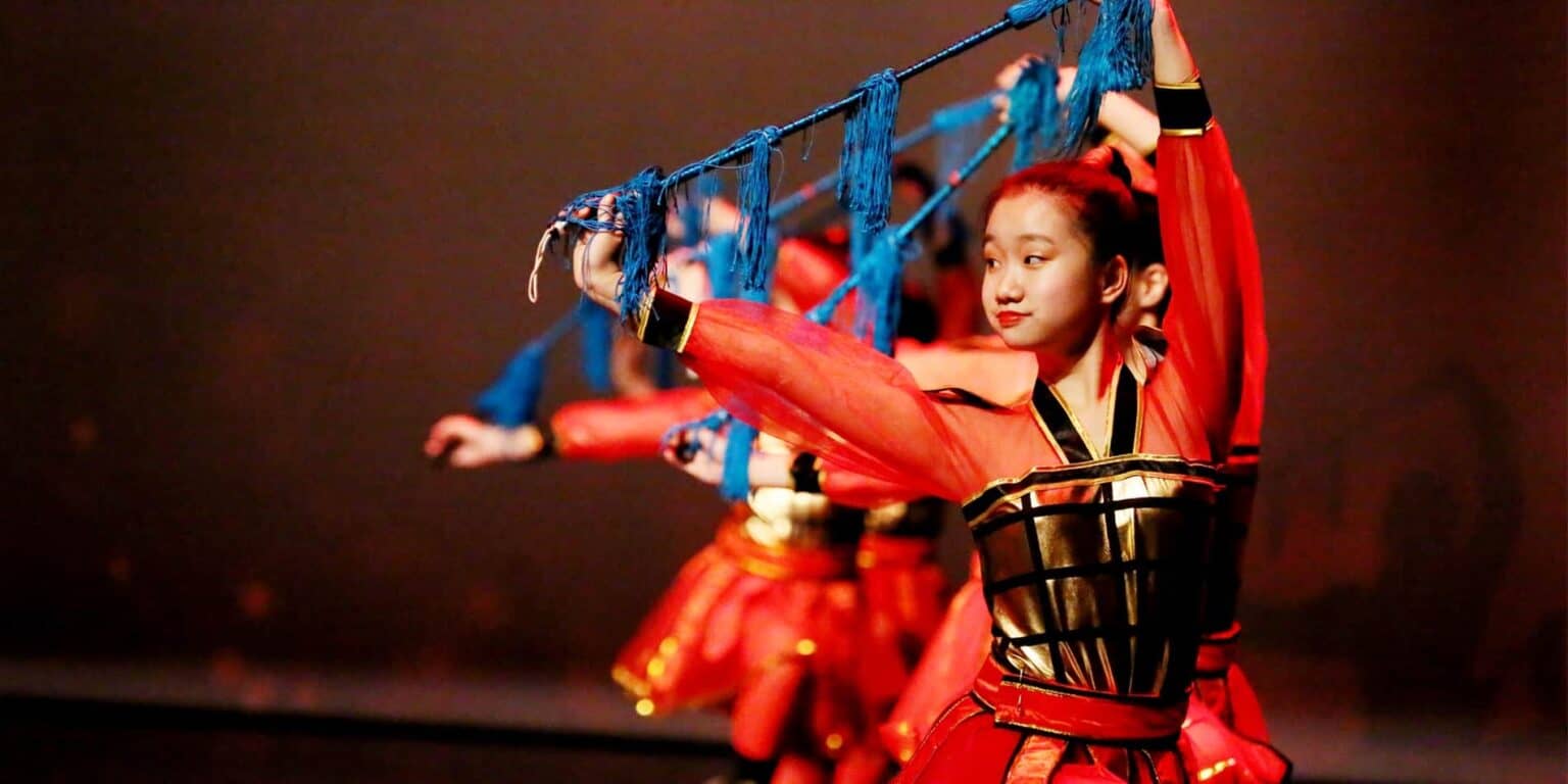Kleurrijke traditionele dansvoorstelling door leerlingen op het podium tijdens World Schools evenement.