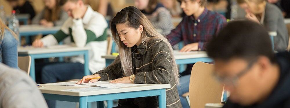 Focused Asian female student taking exam in classroom at World Schools, emphasizing academic excellence and top international education.
