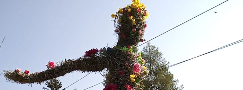 Colorful flower-covered cross-shaped art installation in an outdoor setting.