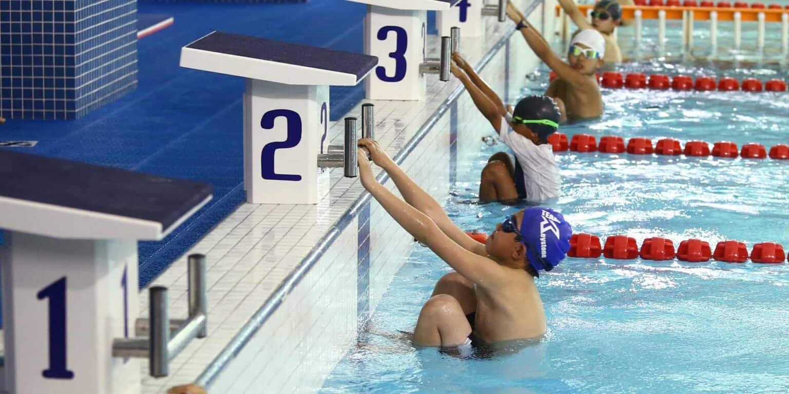 Jonge kinderen zwemmen in een zwembad met winnaarspodia en zwemspullen, ze oefenen in een schools sportevenement.
