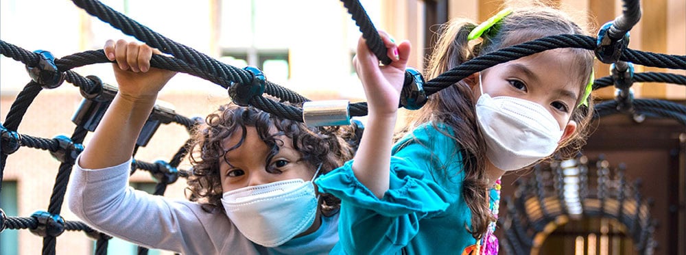 Children wearing face masks playing on outdoor playground equipment at World Schools.