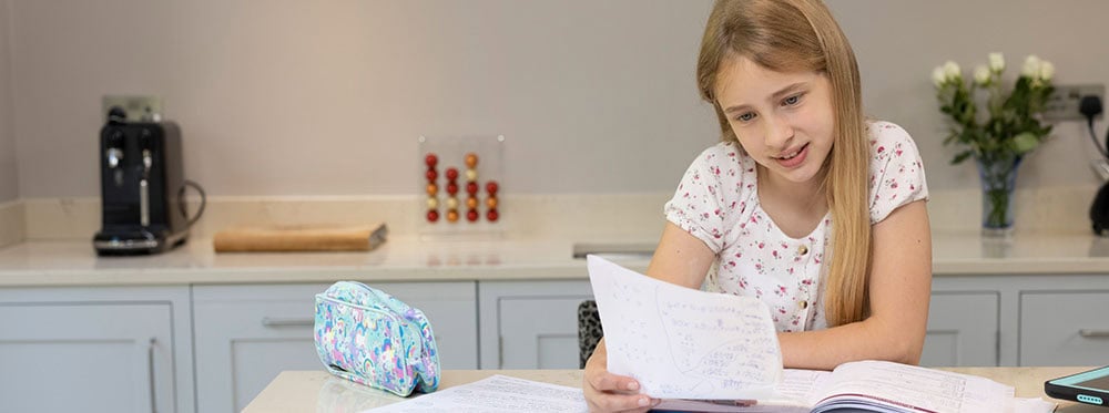 Accessible, cheerful young girl studying at home with school supplies in a bright kitchen environment.