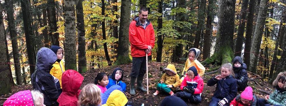 Children exploring nature with a teacher in a forest outdoor classroom educational activity.