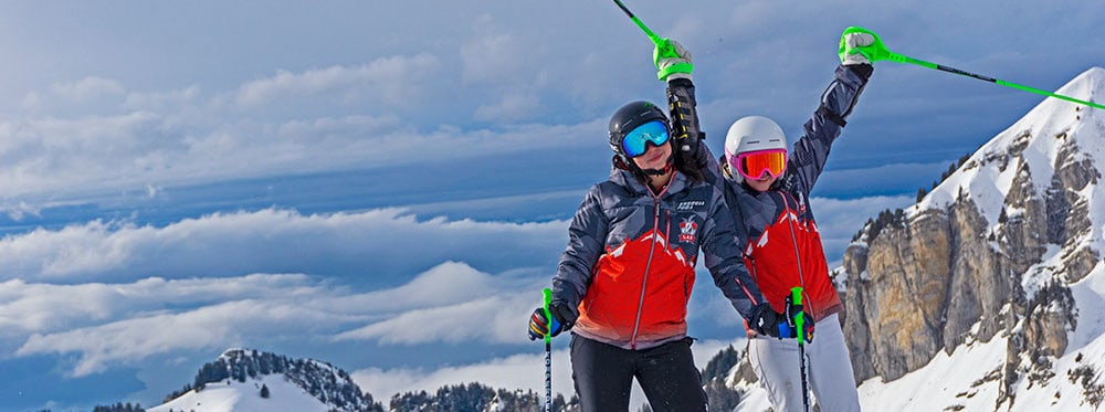 Kids skiing ensemble in snowy mountain landscape with clear blue skies and rugged peaks.