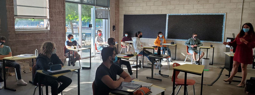 Students in a classroom practicing social distancing, wearing masks, and focusing on learning.