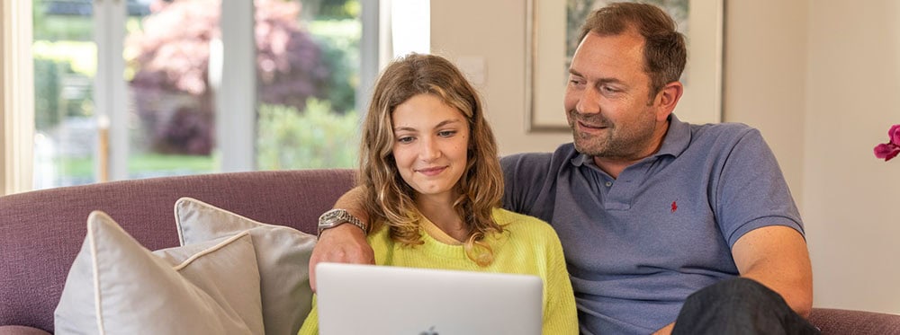 Engaged father and daughter exploring online learning on laptop at home, promoting educational growth.