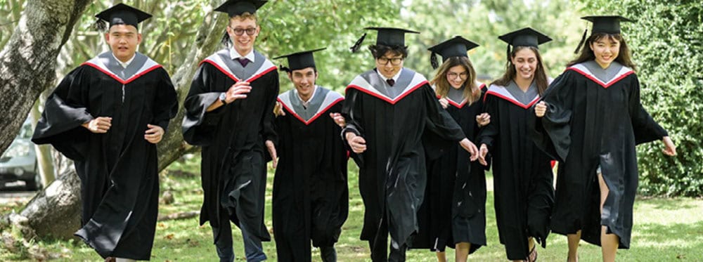 Graduates in academic gowns celebrating outdoors at a school graduation ceremony for elite international students from World Schools.