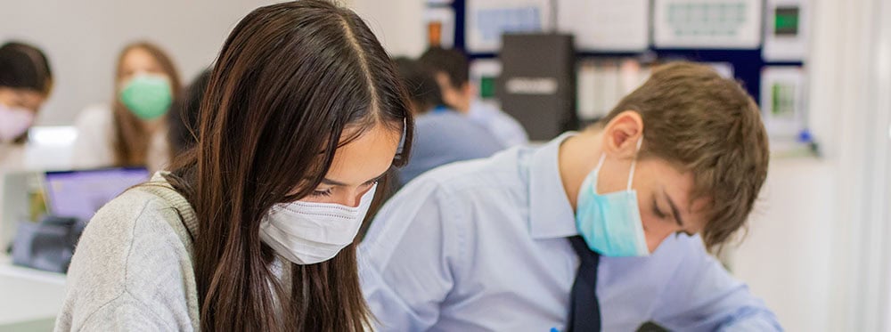 1. Students wearing masks in a modern classroom focusing on experiential learning.