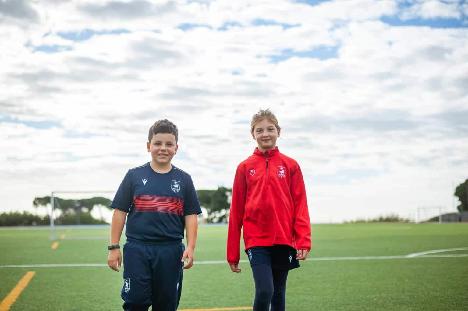 1. Bambini in divisa sportiva in piedi in un campo sportivo di una scuola, sotto un cielo nuvoloso.