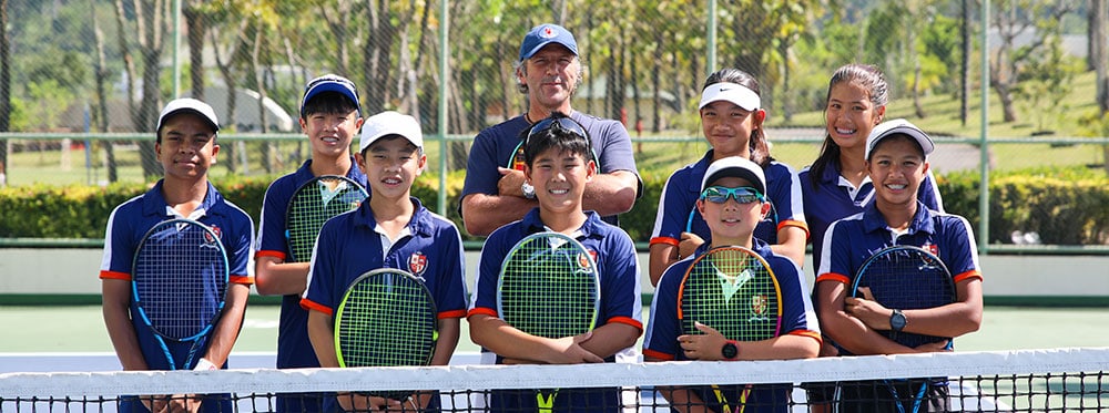 Young students with tennis rackets and coach on outdoor tennis court, promoting sports and extracurricular activities in world schools.