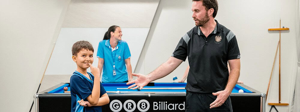 Friendly boy enjoying billiards lesson at a world-school sports activity.