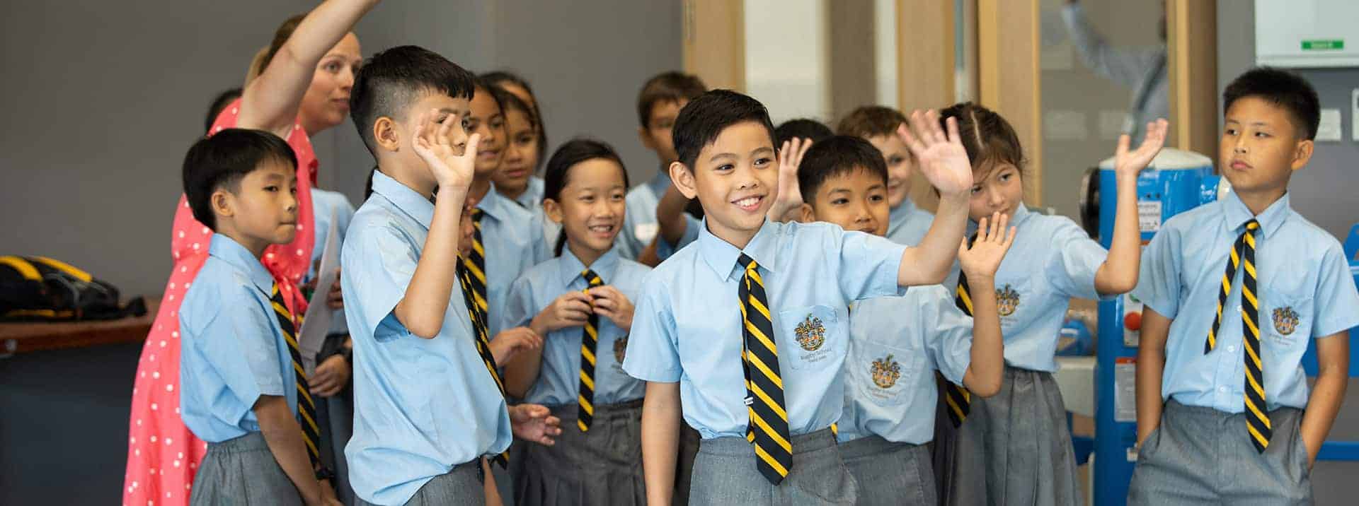 Engaging group of diverse students in school uniform raising hands in classroom.