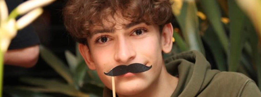 Young student with playful mustache pet mask at World Schools campus during outdoor activities.