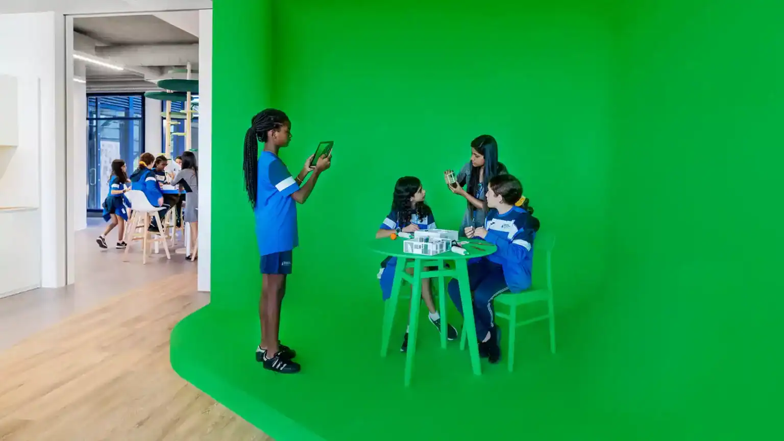 Students engaging with educational technology in a modern classroom with a green screen background at a world school.