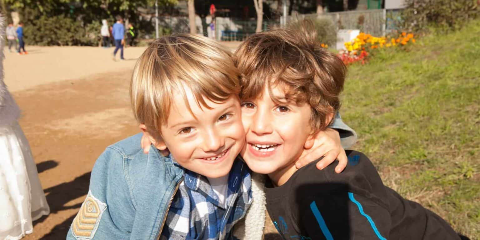 Happy children hugging outdoors at a school playground, promoting friendly school environment and student happiness.