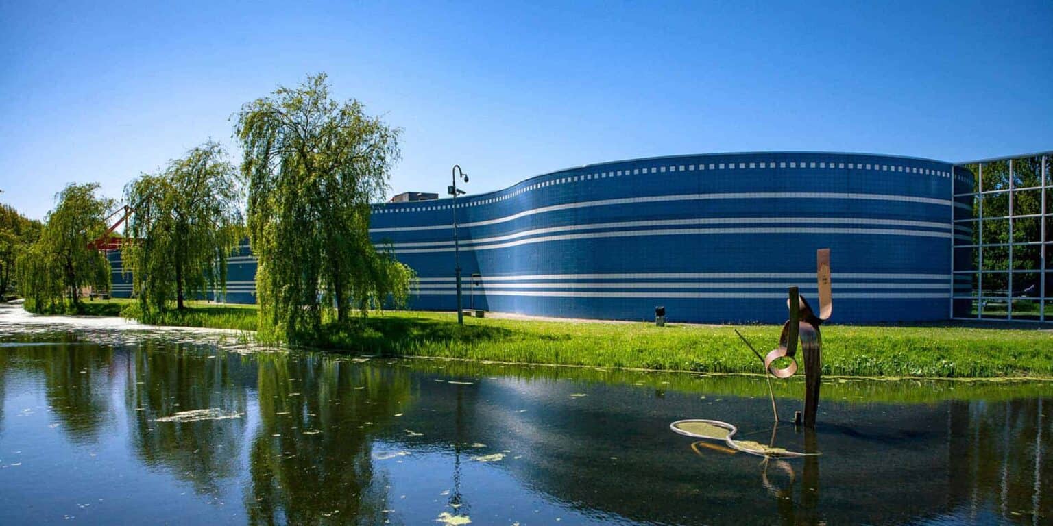 Modern blue school building with water features, surrounded by greenery and trees, in a scenic outdoor setting.