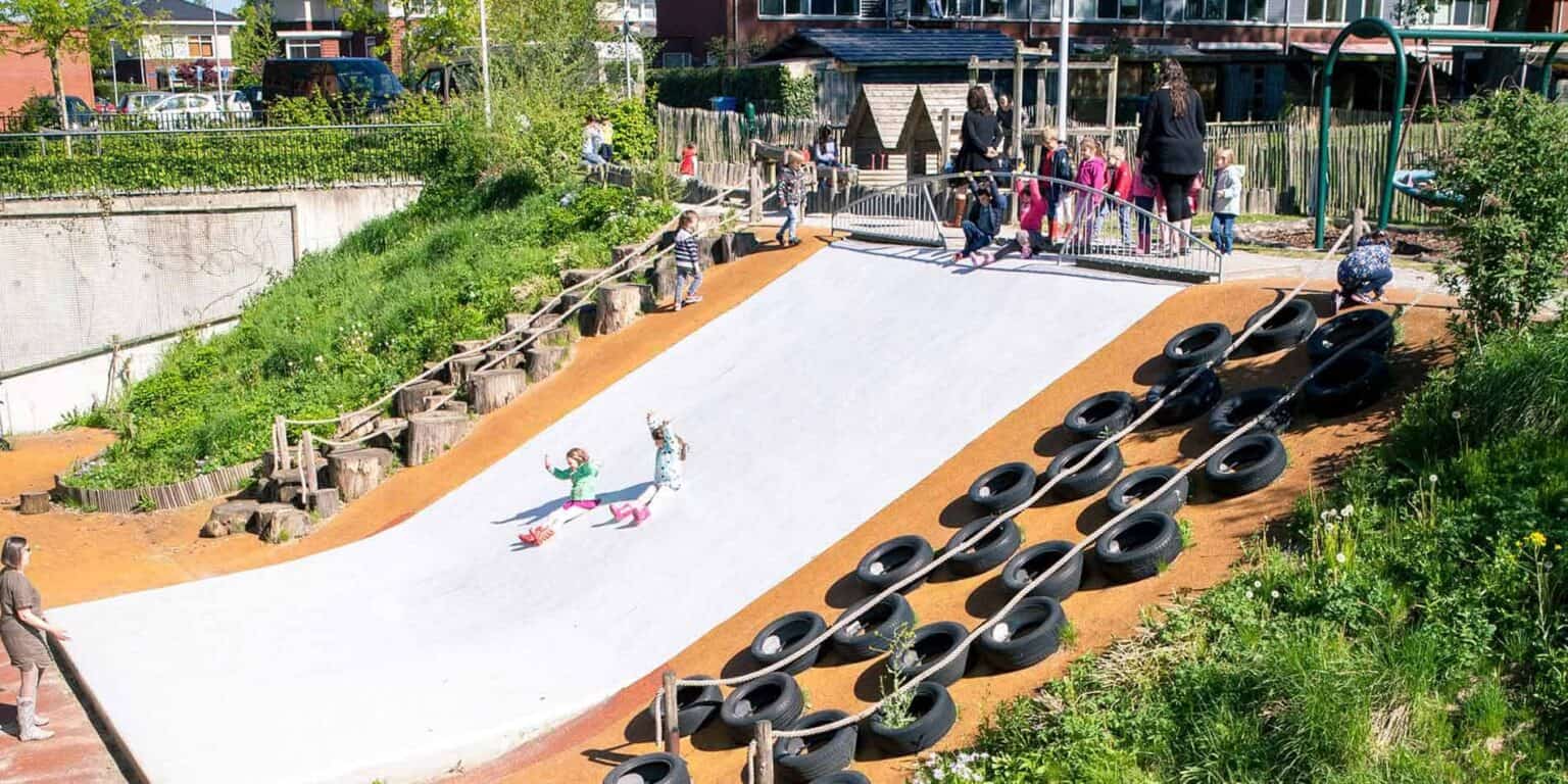 Colorful outdoor playground at a world school with children playing and teachers supervising.