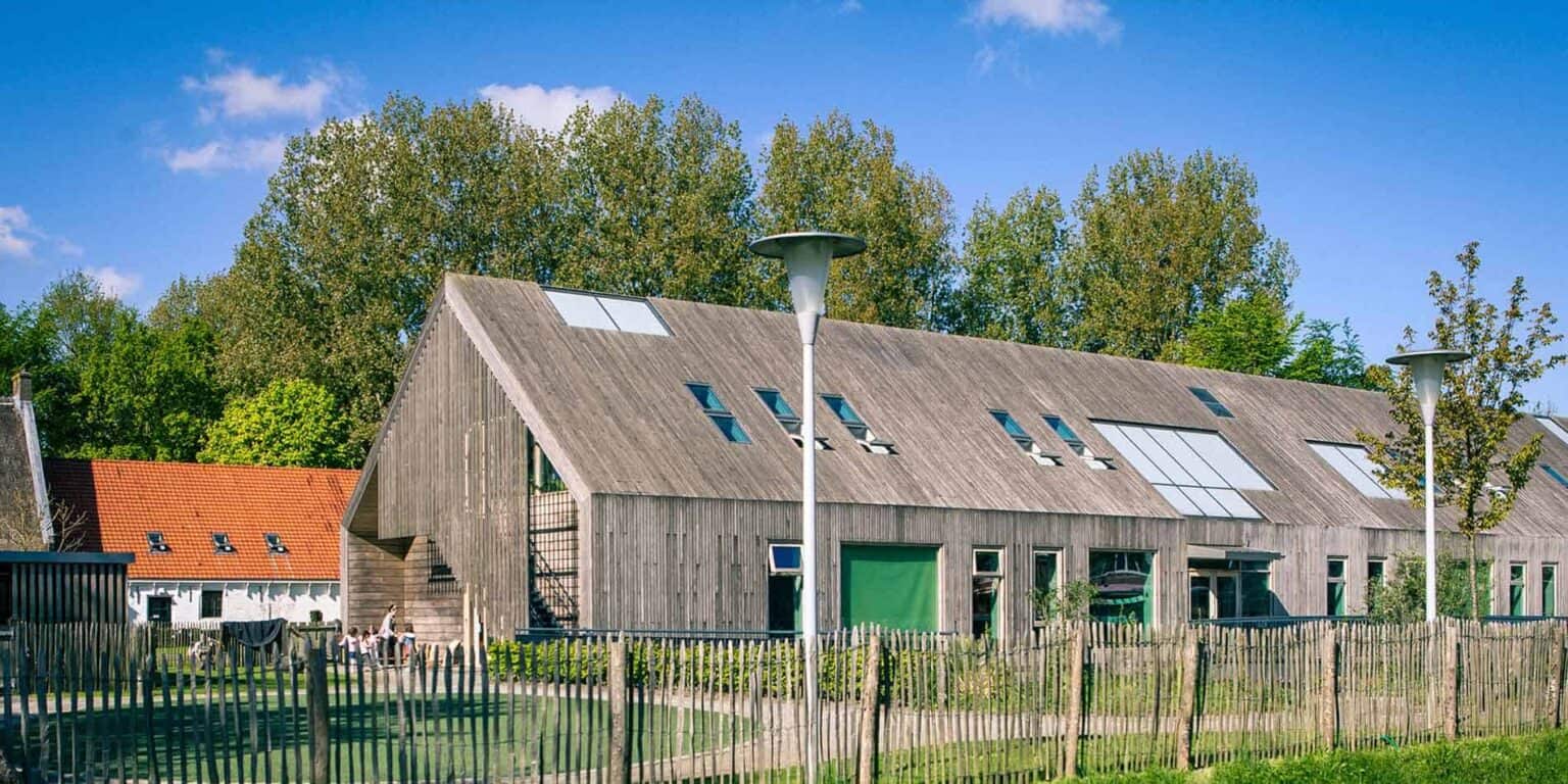 Modern eco-friendly school building with wooden architecture, surrounded by greenery and blue sky.