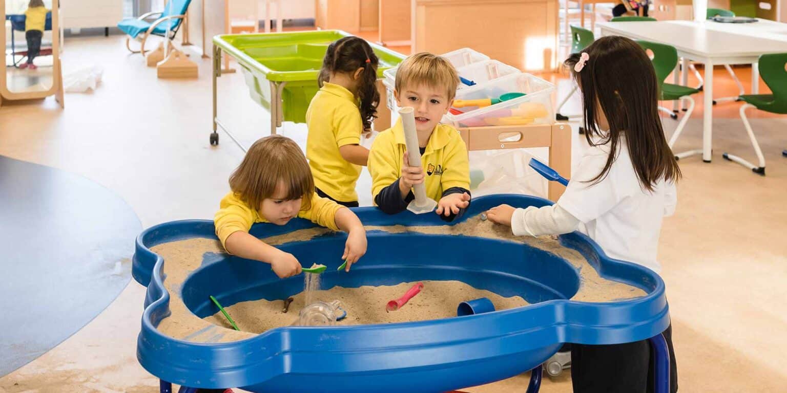 明亮的学龄前儿童在带有感官沙盘的现代化教室里玩耍和学习。.