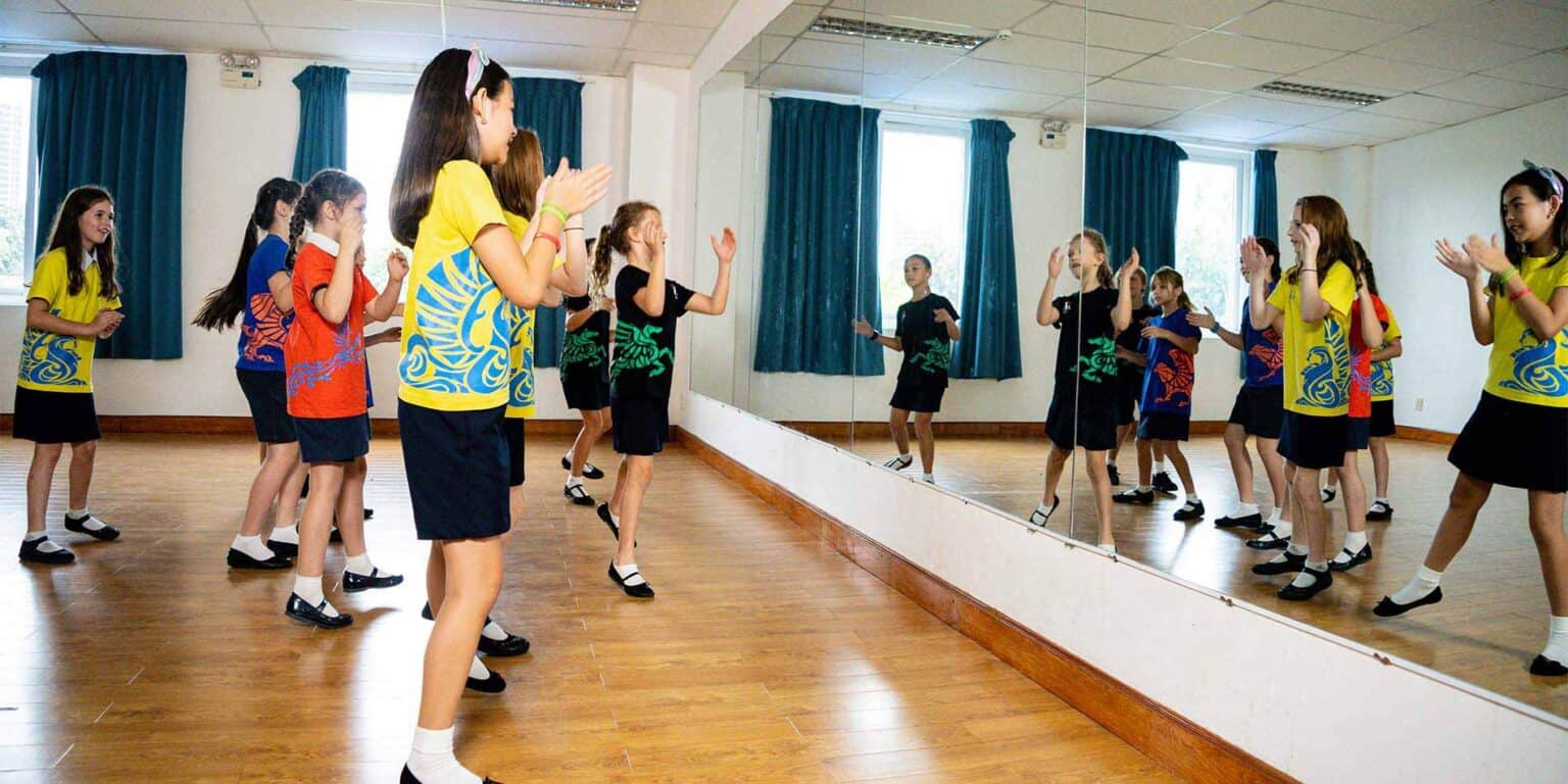 Brightly dressed students practicing dance in a school studio with mirror walls, promoting creativity and holistic education.