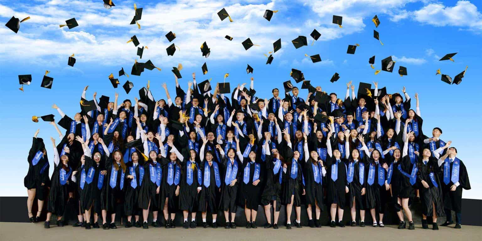 Graduate students celebrating graduation ceremony at World Schools; diverse students in caps and gowns throwing caps in the air, under blue sky.