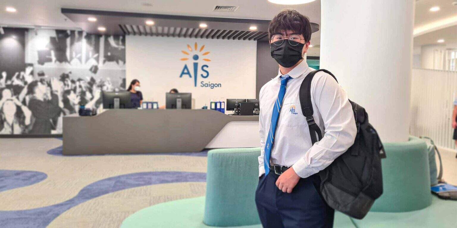 Young student in school uniform with backpack at AIS Saigon reception area.
