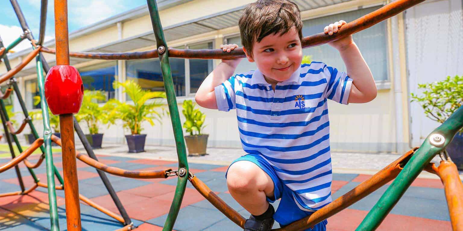 Bright young boy playing on outdoor playground at a world school, engaging in active learning and recreation.