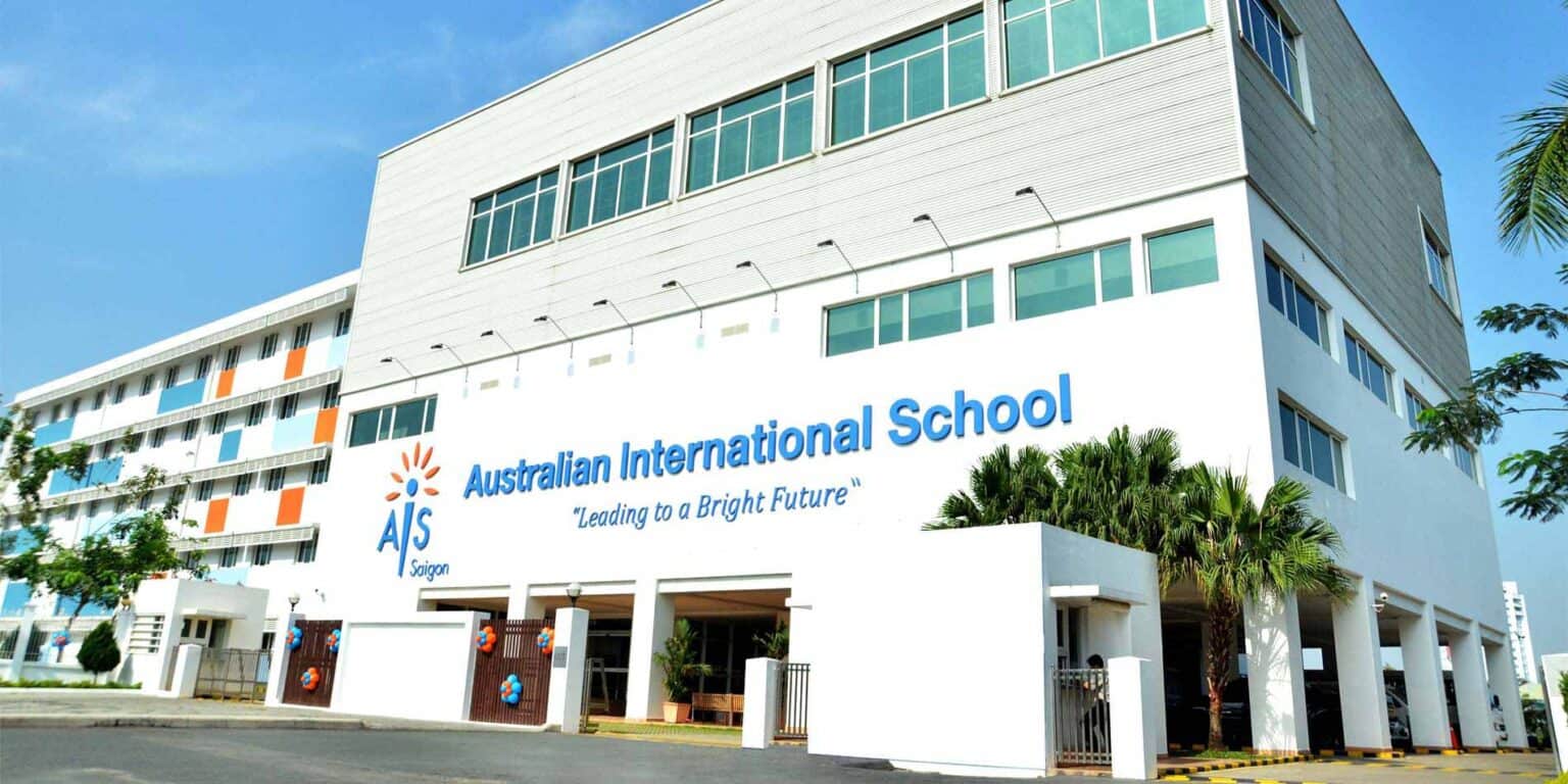 Modern Australian International School building in Saigon with vibrant blue and orange signage, lush palm trees, and clear sky.