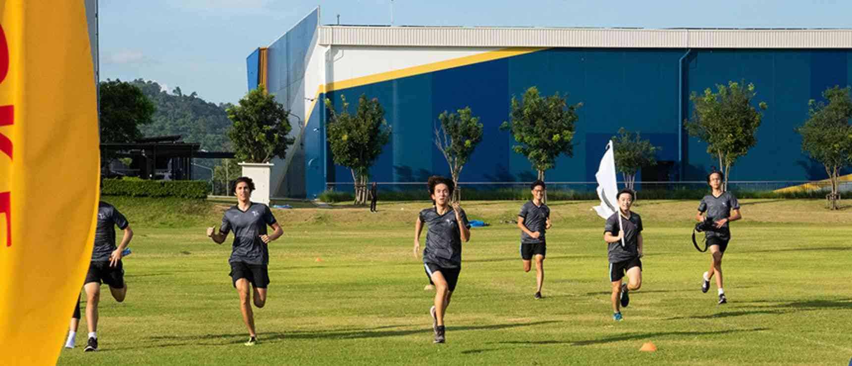 Young students running on school sports field engaging in outdoor physical activity.
