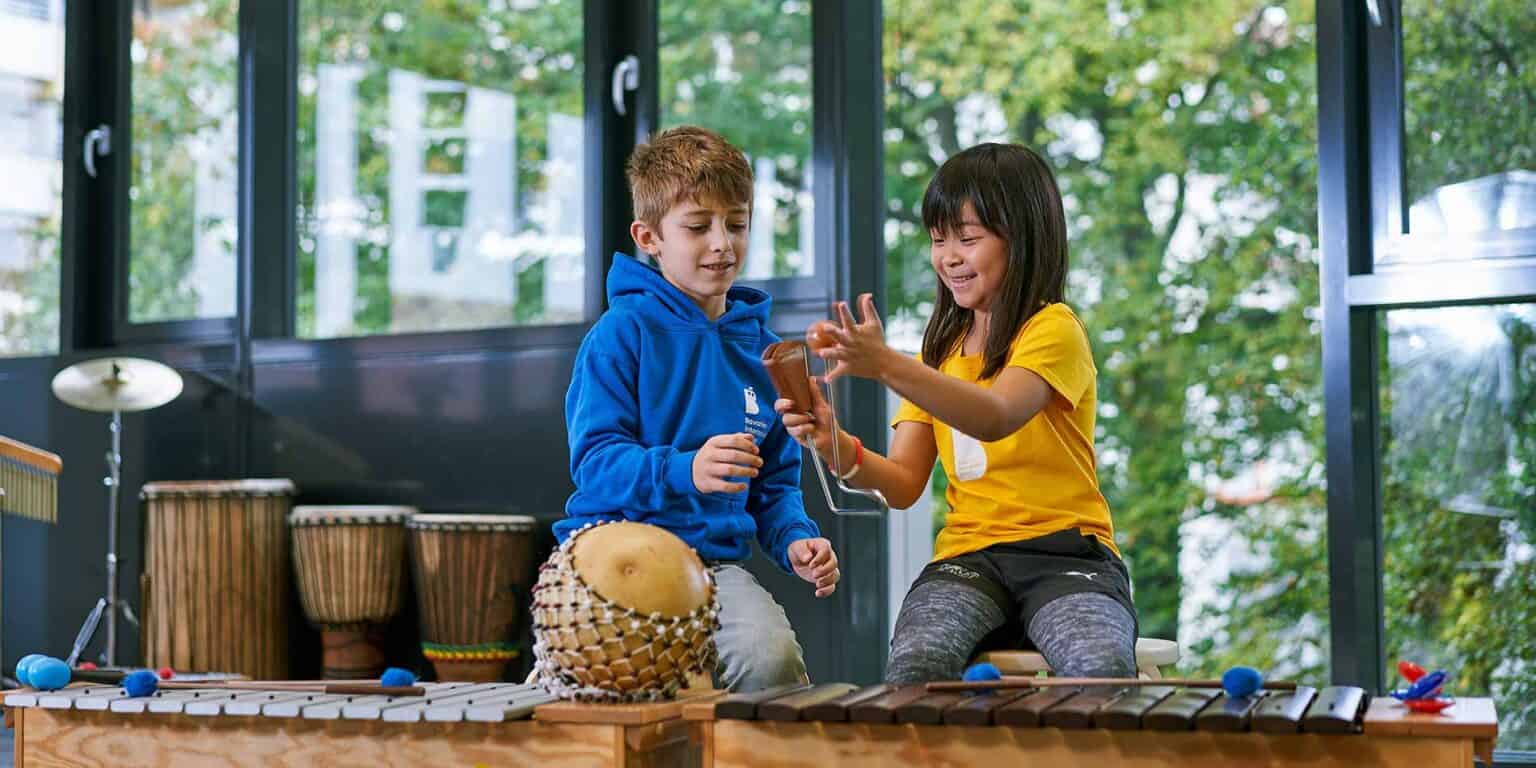 Colorful children playing musical instruments in a bright, modern classroom at a world school.