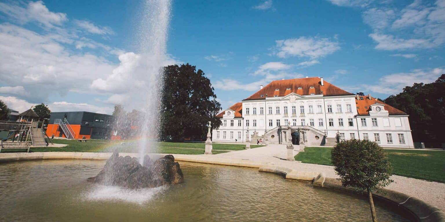 Brightly lit historic building with a fountain and park, symbolizing prestigious international schools.