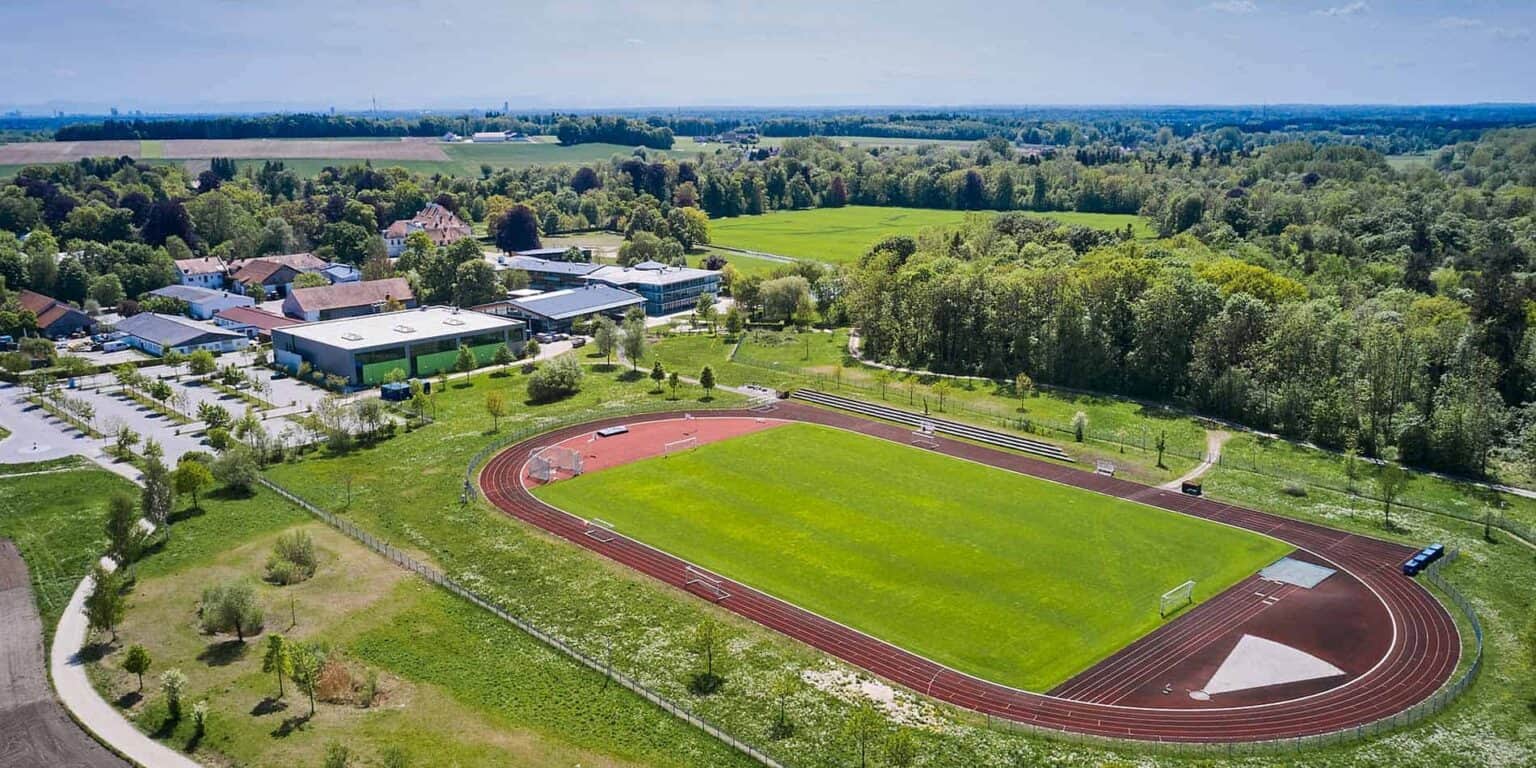 Modern school campus with sports track and green outdoor areas in a scenic setting.
