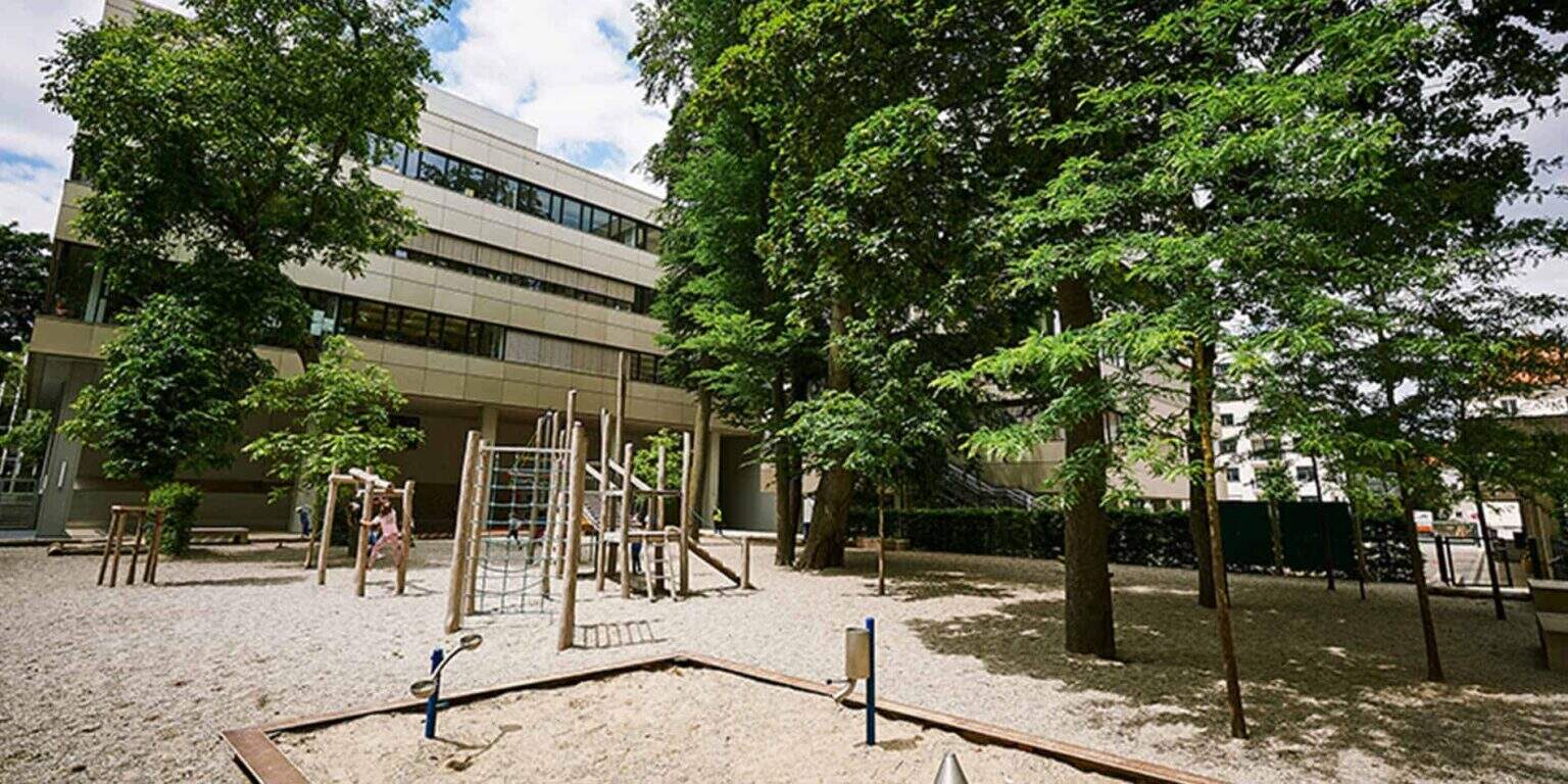Modern school building with outdoor playground and lush trees for optimal student learning environment.