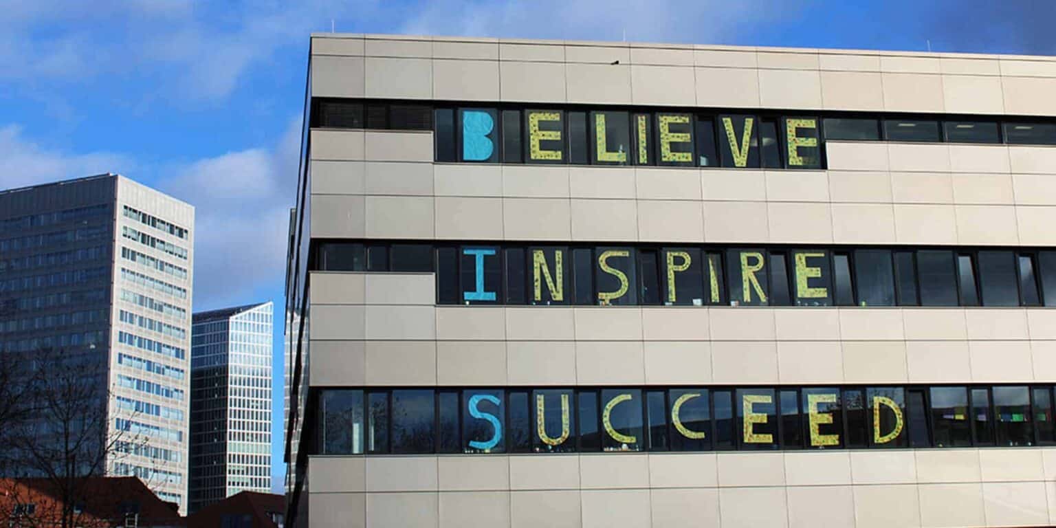 Diverse modern office building with inspirational message “Believe, Inspire, Succeeded” displayed on windows, in a business district skyline.