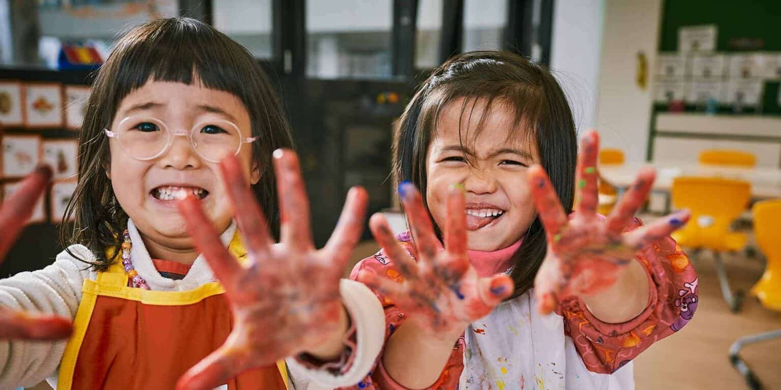 Happy children with painted hands having fun in a school classroom, promoting creative learning environments.