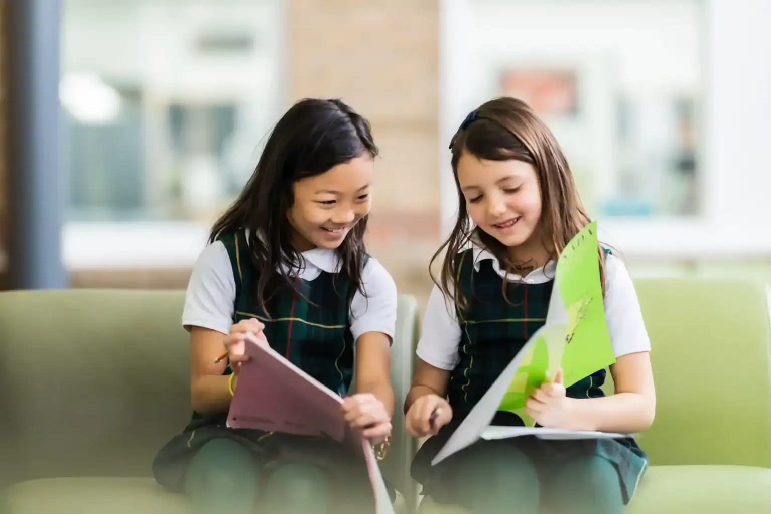 Young schoolgirls reading books together in a modern school waiting area, promoting international education and student collaboration.