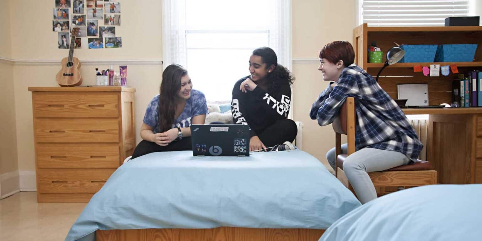 Young students studying and chatting in a cozy dorm room with laptops at a world school.